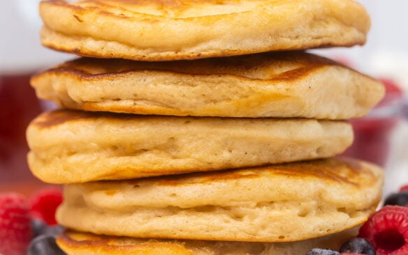 buttermilk pancakes stacked high on a white plate with berries around.