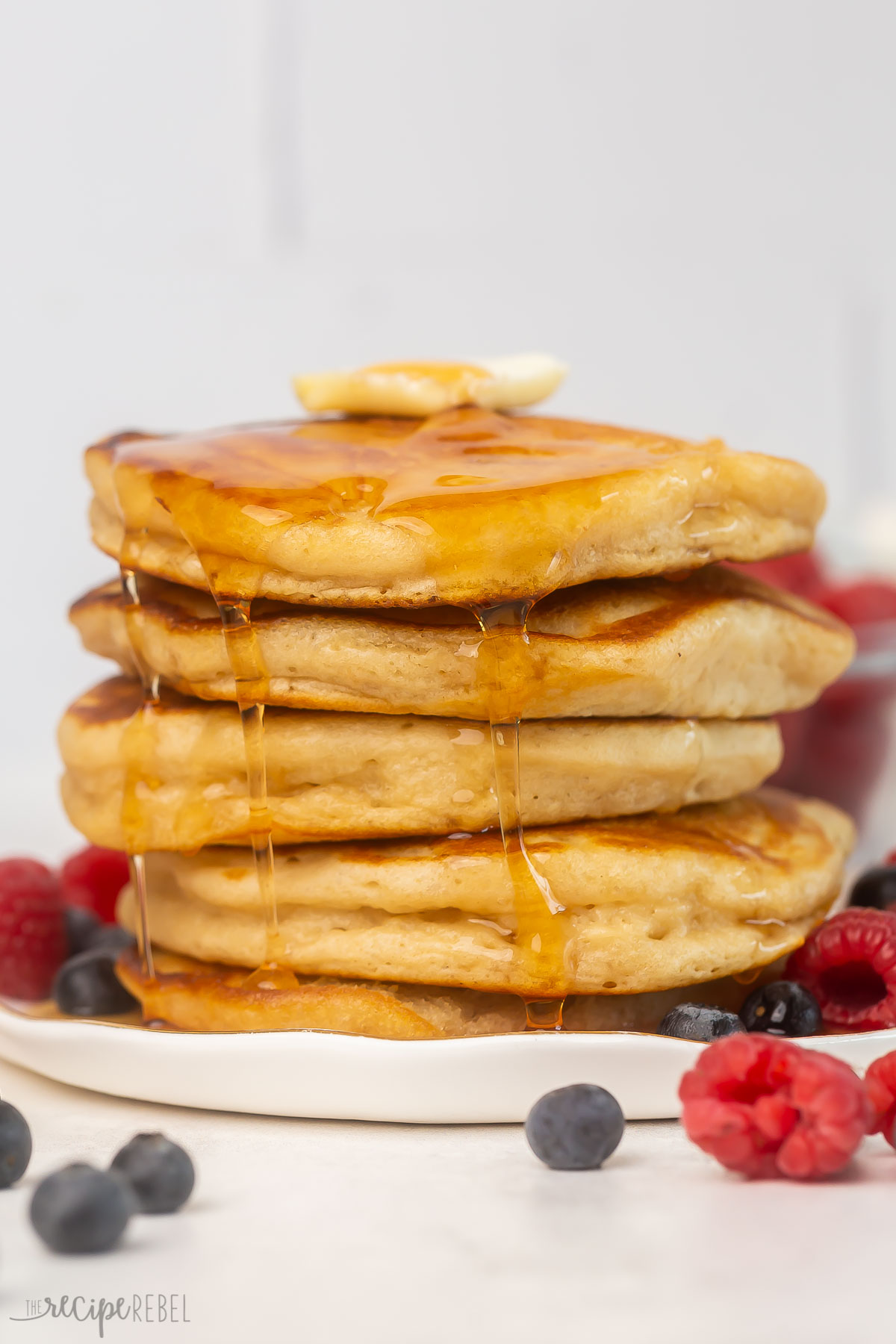 stack of golden pancakes with syrup running down the sides and butter on top.