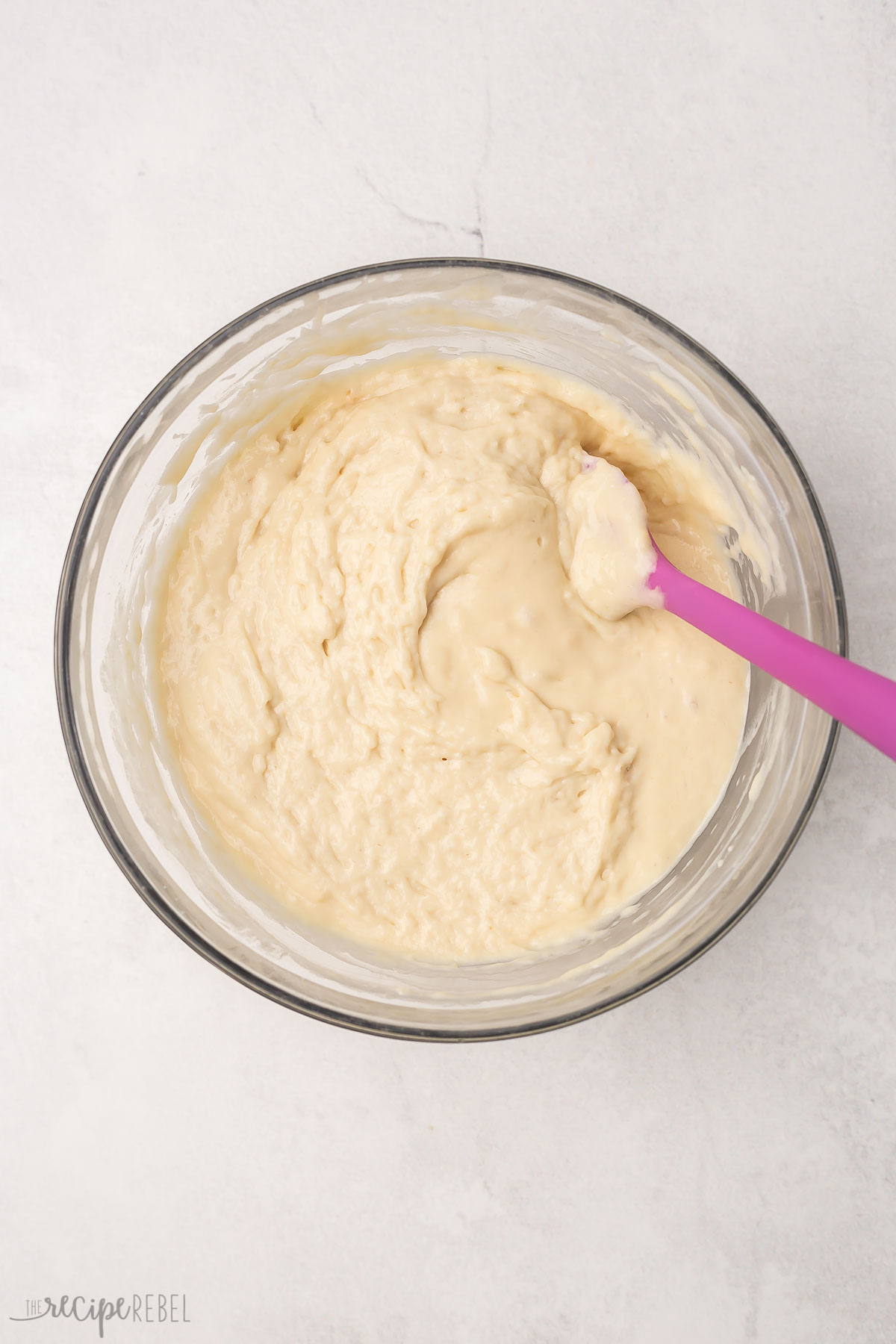 mixed buttermilk pancake batter in glass bowl and purple spatula.