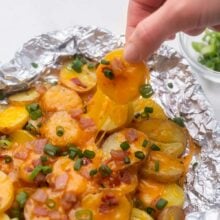 hand pulling a cheesy grilled potato out of foil pack.