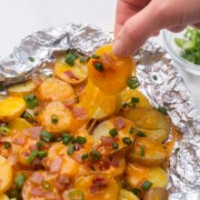 hand pulling a cheesy grilled potato out of foil pack.