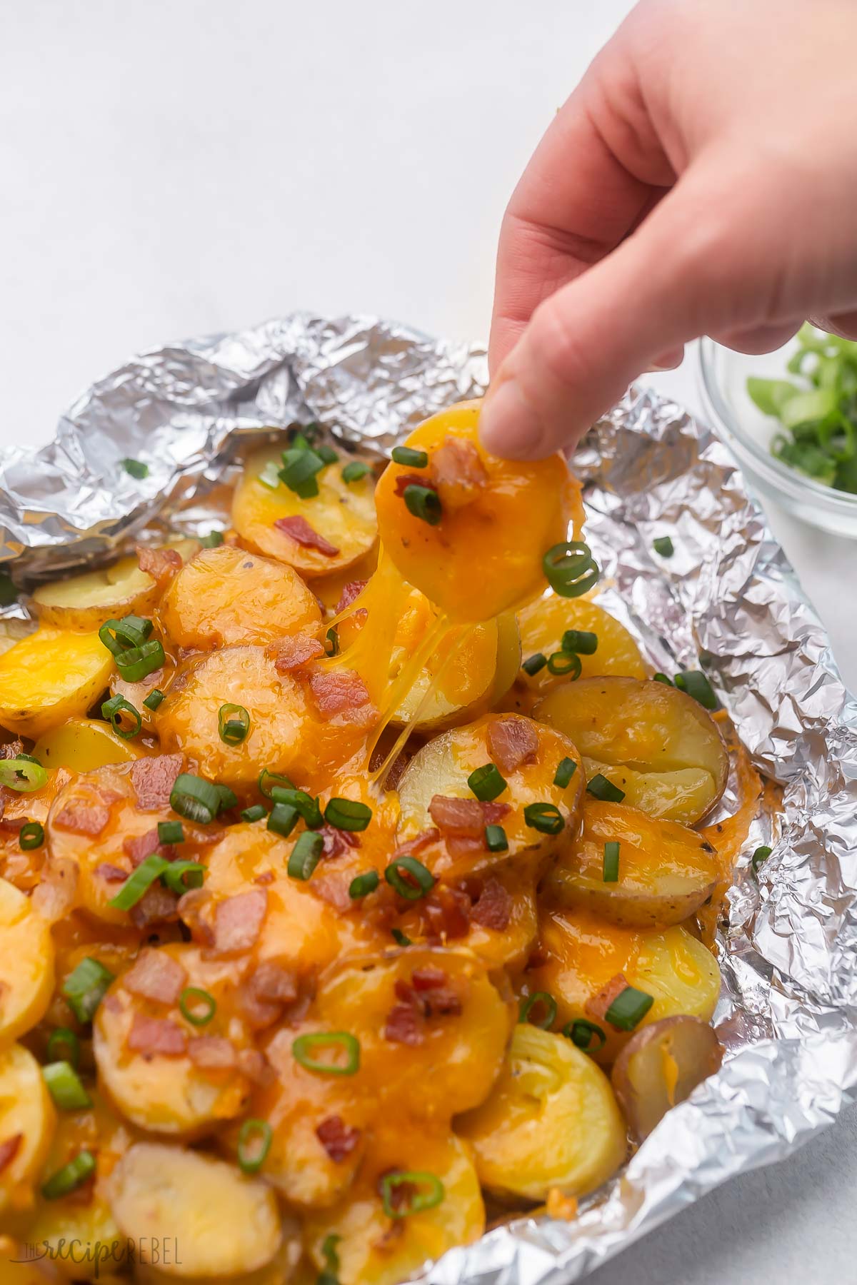 hand pulling a cheesy grilled potato out of foil pack.