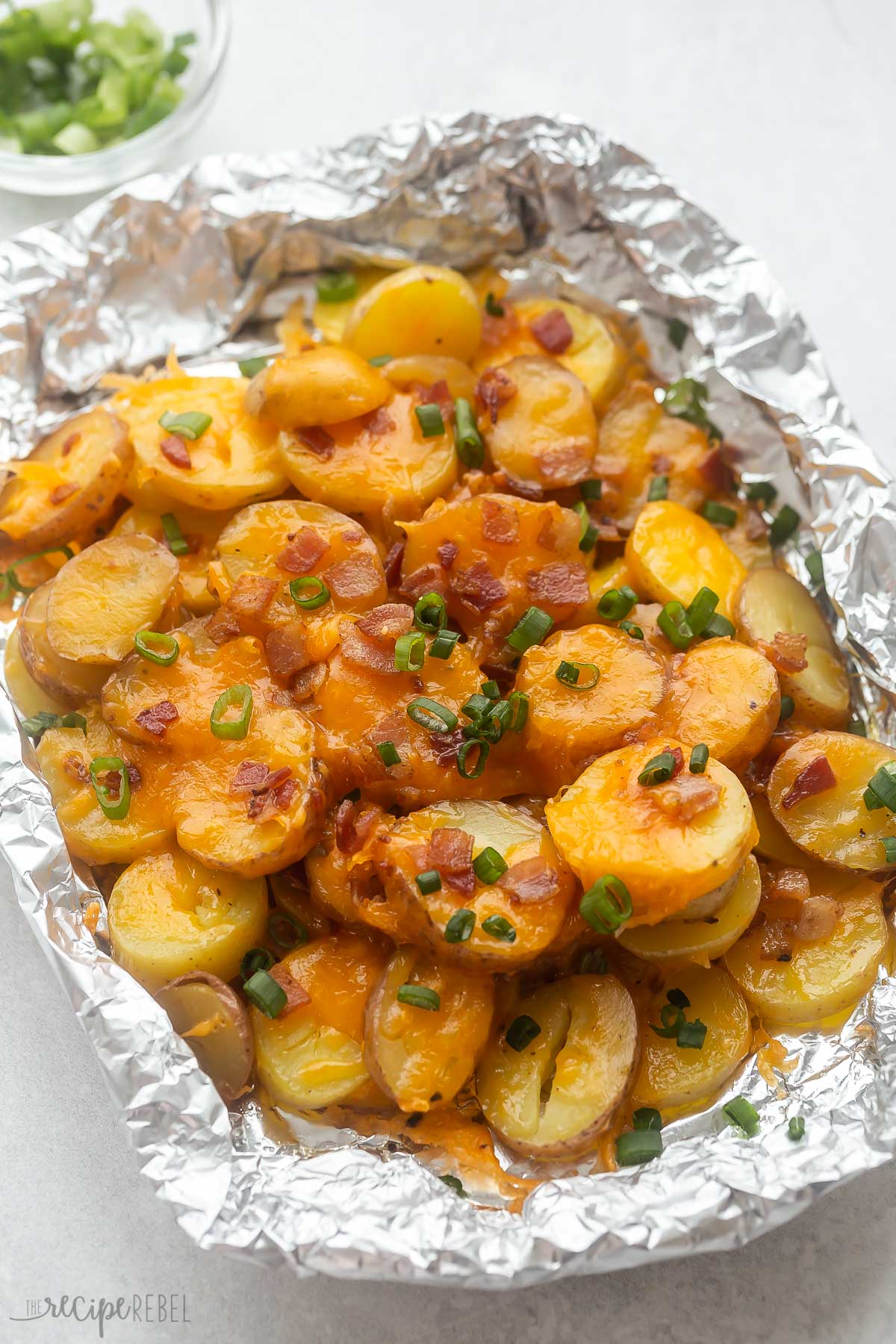 cheesy grilled potatoes in a foil pack with bacon and green onions on top.