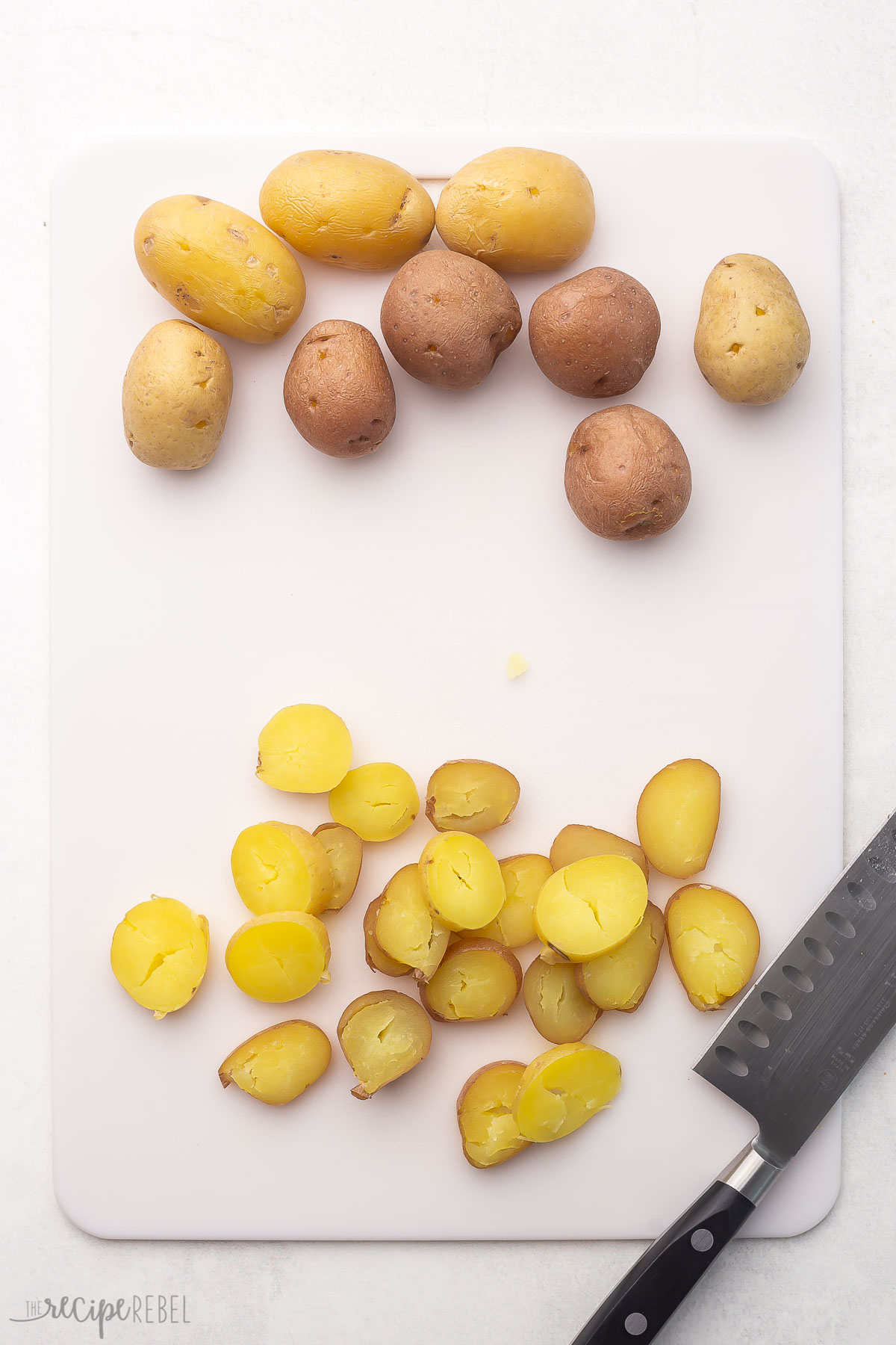 white cutting board with knife and small potatoes cut in slices.