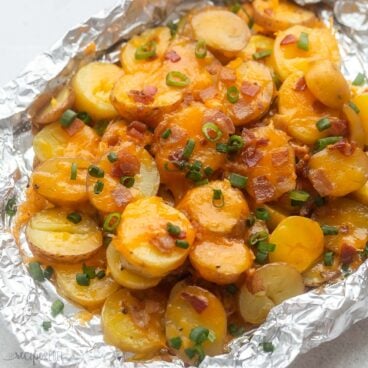 close up view of foil pack with grilled potatoes covered in melted cheese, bacon, and green onions.