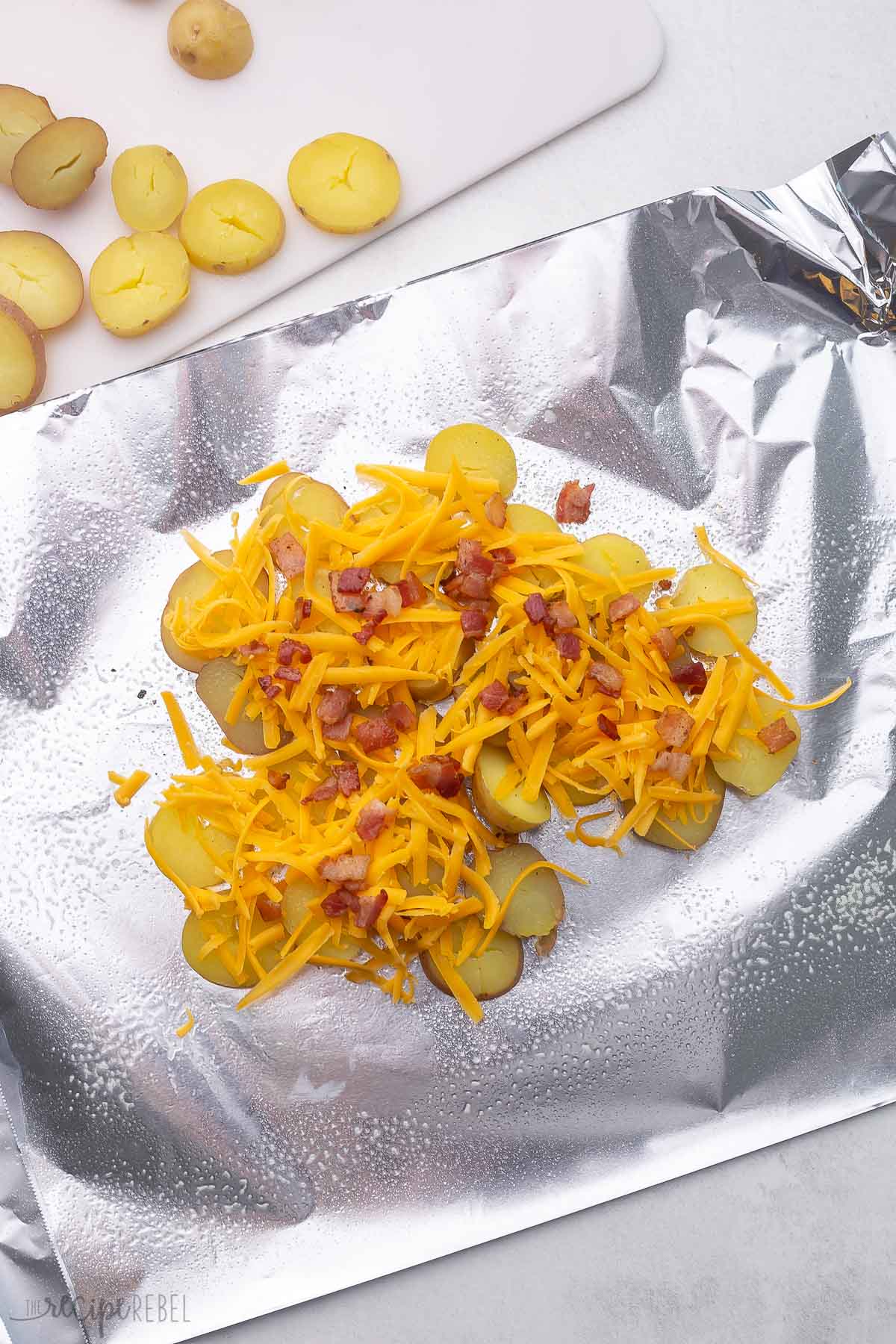 aluminum foil with sliced potatoes covered in shredded cheese and bacon bits.