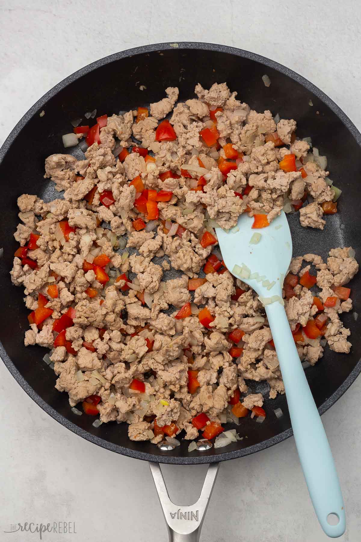 ground chicken and peppers cooking in a black frying pan.