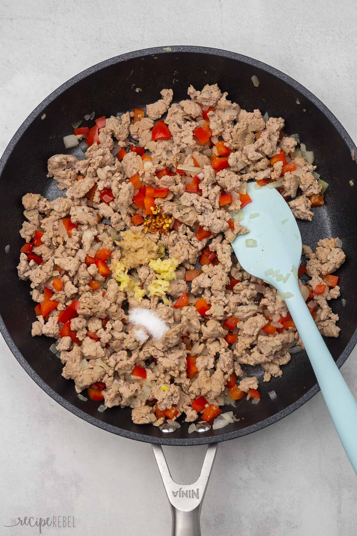 black frying pan with cooked chicken, peppers, and spices added.