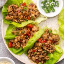 three chicken lettuce wraps lying on a plate with chopped green onions beside.