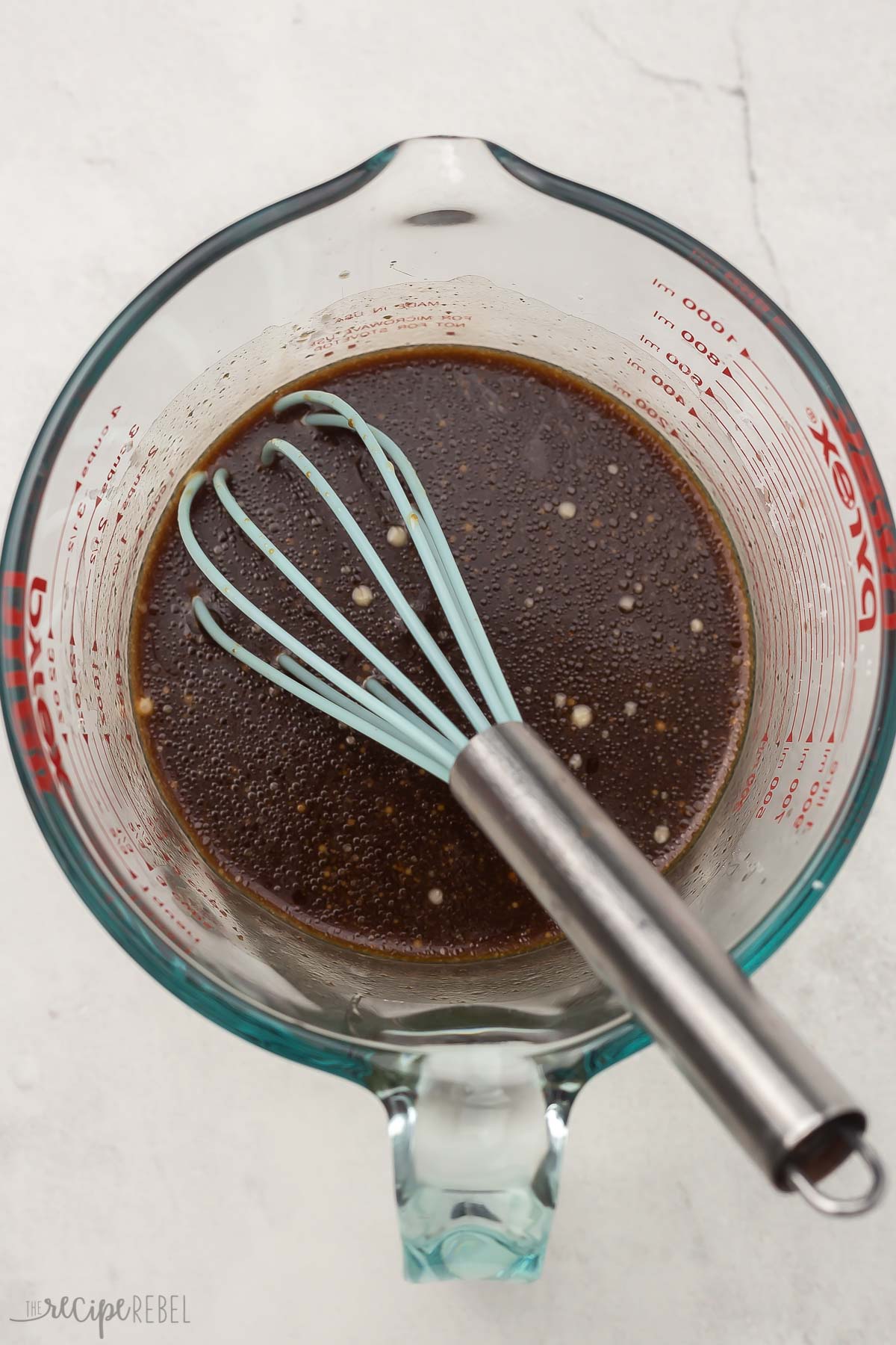 overhead view of glass measuring cup with sauce ingredients and whisk in it.