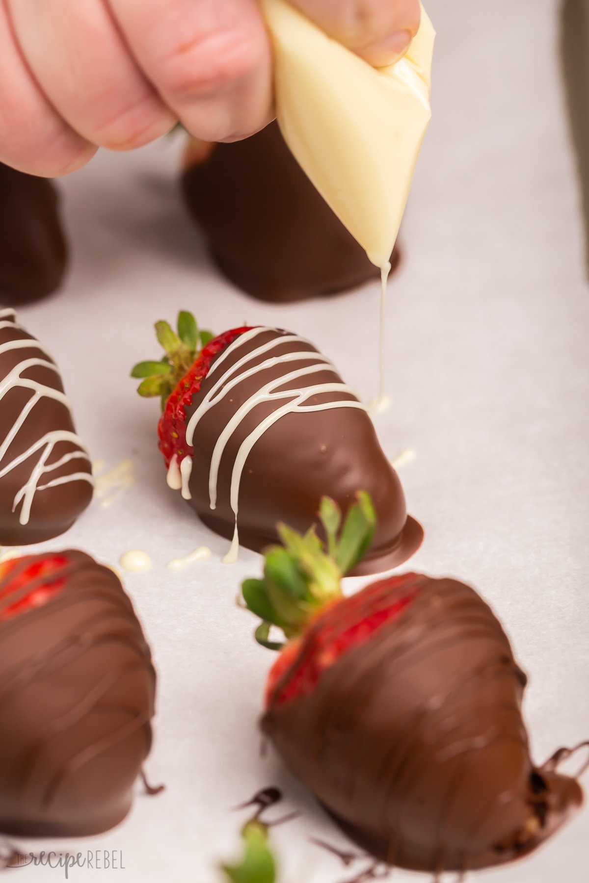 Decorating a chocolate covered strawberry with white melted chocolate.