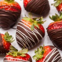 Top view of chocolate covered strawberries on a white plate drizzled with white and brown chocolate.