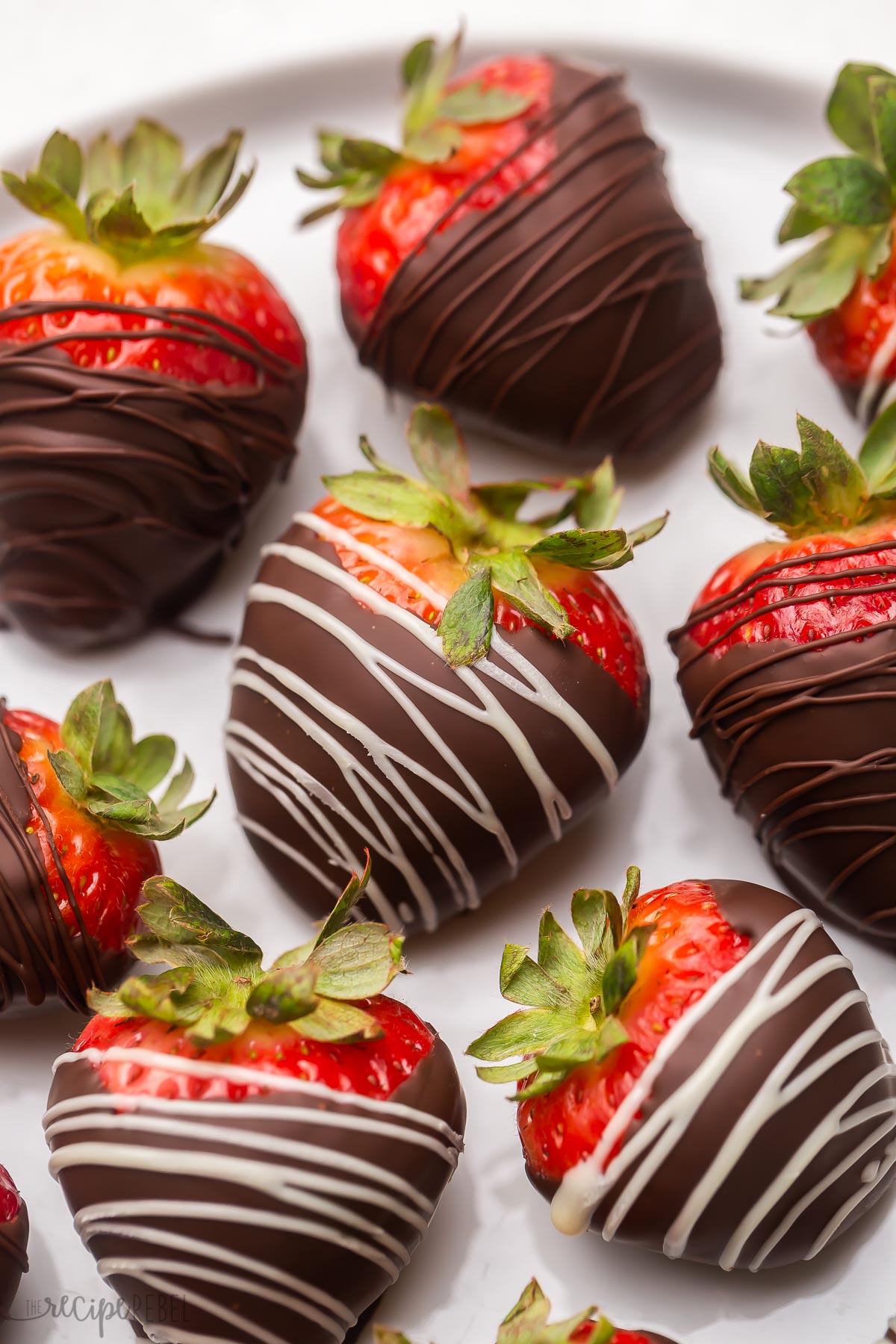 Top view of chocolate covered strawberries on a white plate drizzled with white and brown chocolate.