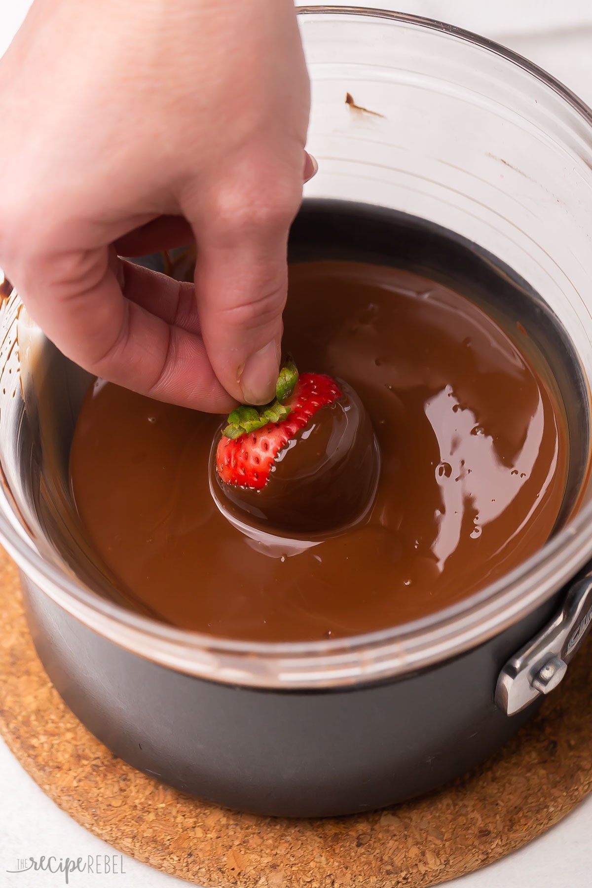 Dipping a strawberry into a bowl of melted chocolate.