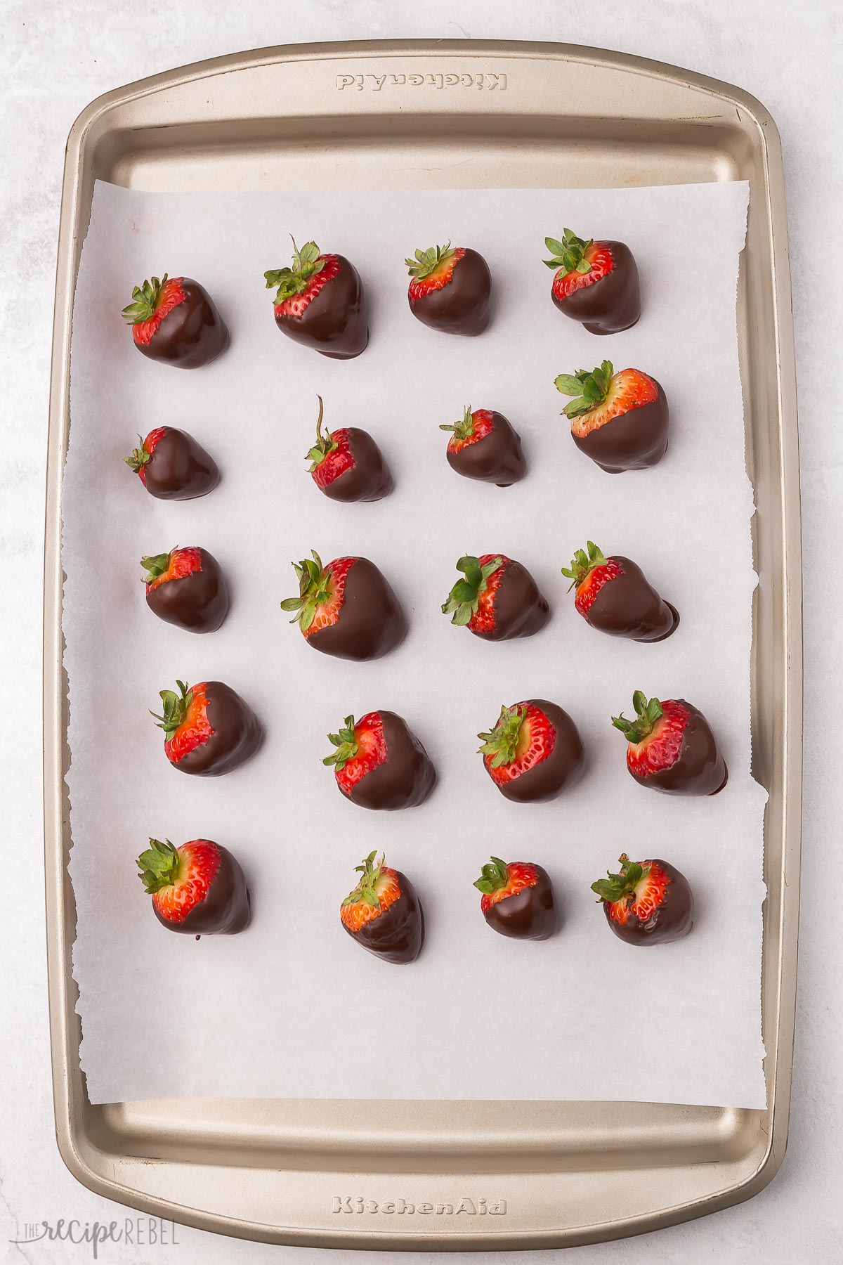 Top view of a pan full of chocolate covered strawberries on parchment paper.