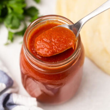 jar of enchilada sauce with spoon scooping some out.