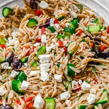 Top view of Greek Pasta Salad in a pasta bowl with someone holding a fork in it.