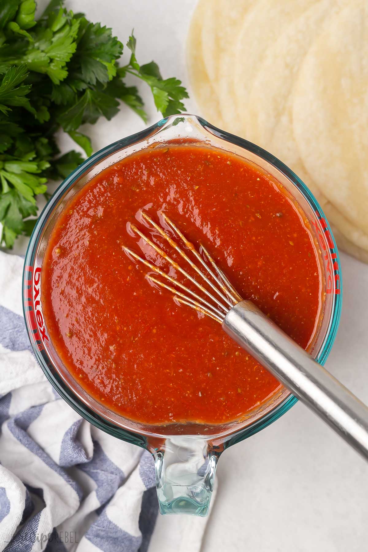 large glass measuring cup of enchilada sauce with whisk.