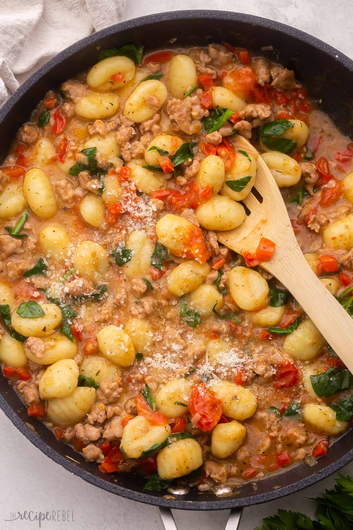 Top view of gnocchi in a black pan with a wooden spoon in it. 