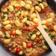 Top virew of Gnocchi with Sausage and Tomatoes in a pan with a wooden spoon in it.