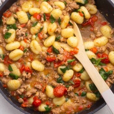 Top virew of Gnocchi with Sausage and Tomatoes in a pan with a wooden spoon in it.