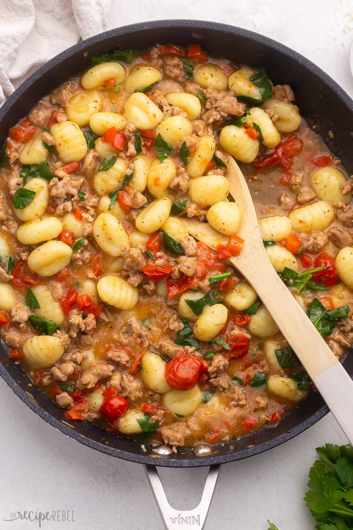 Top virew of Gnocchi with Sausage and Tomatoes in a pan with a wooden spoon in it. 