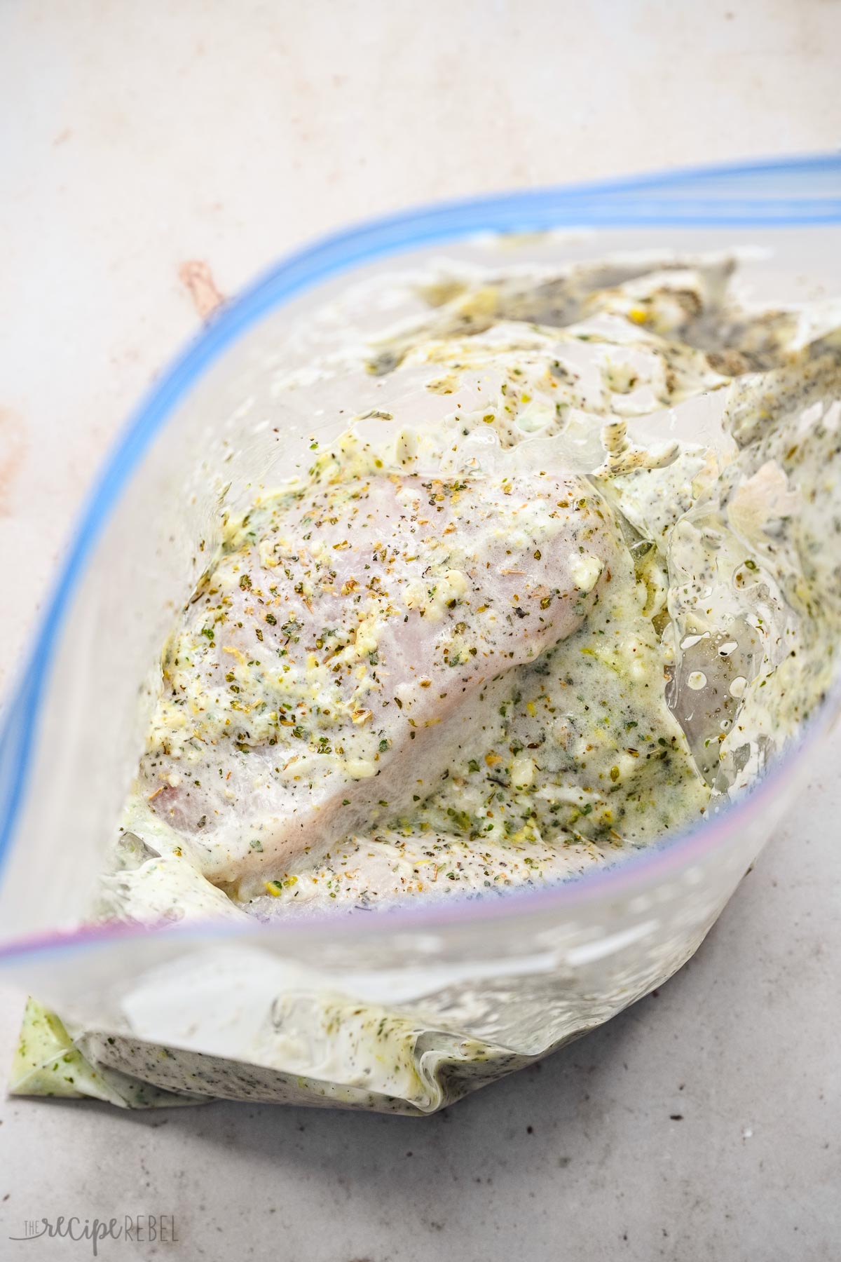 Top view of an open Ziploc bag with marinade ingredients and raw chicken breasts in it. 