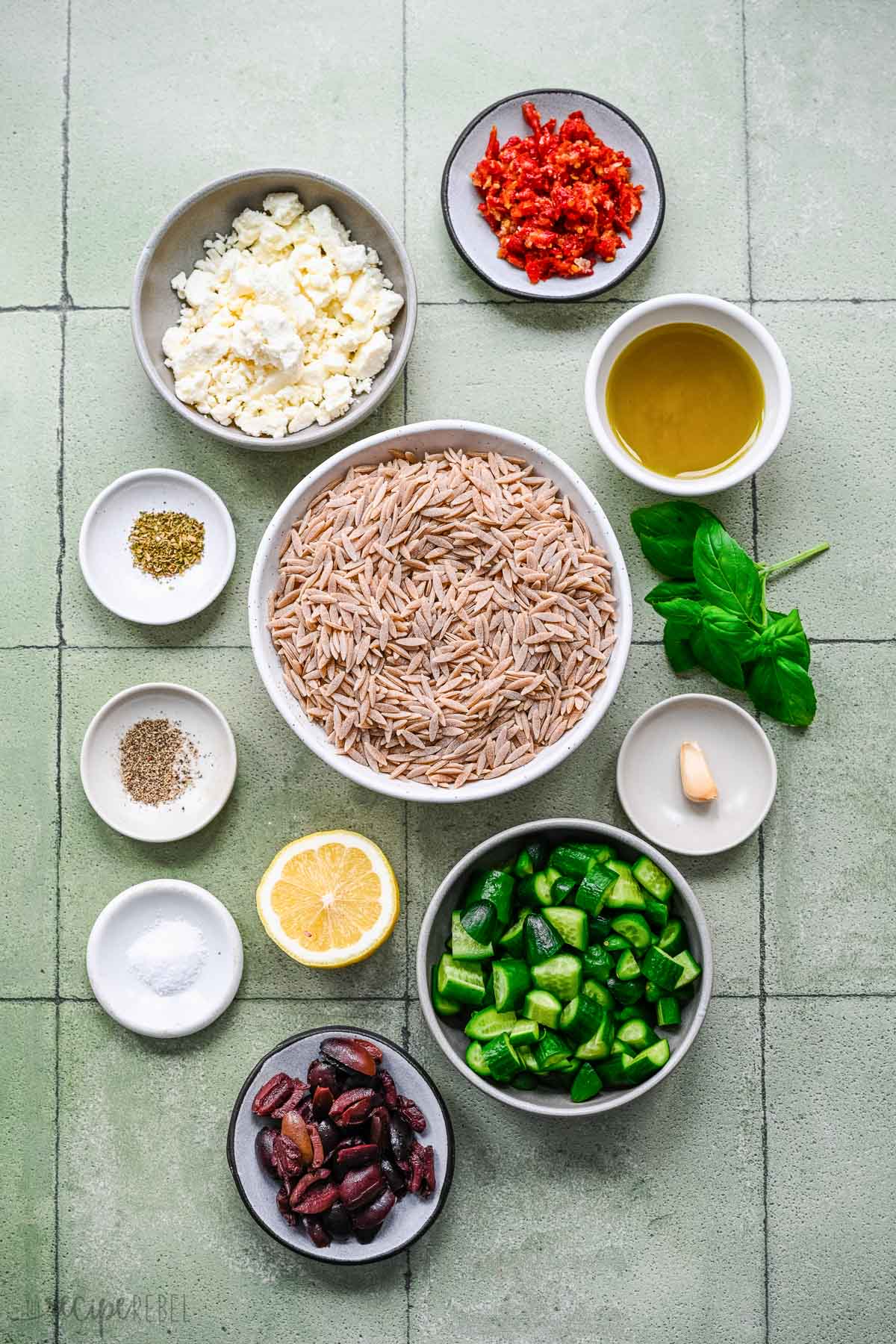 Top view of ingredients needed to make Greek pasta salad in small bowls.