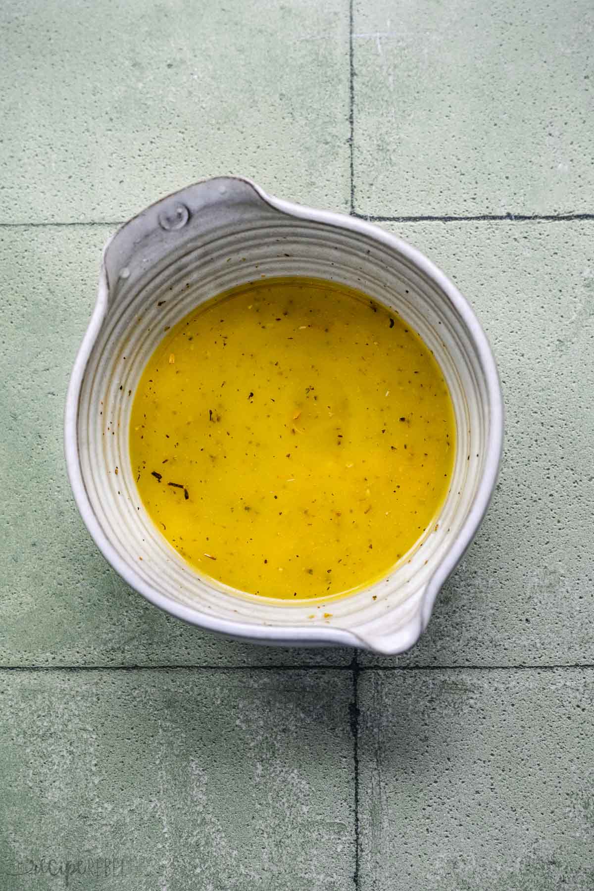 Top view of homemade Greek salad dressing in a white mixing bowl. 