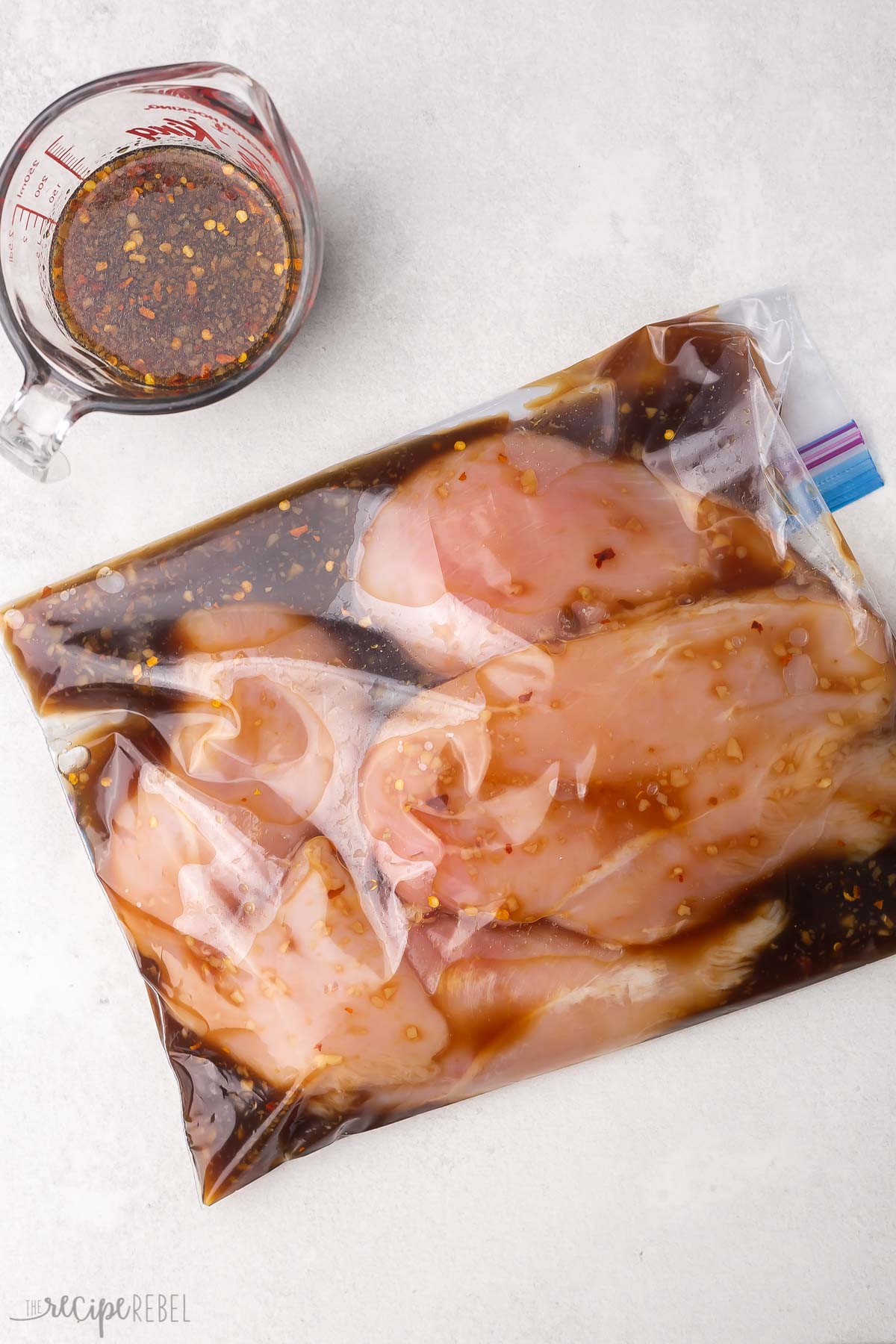 sealed bag with chicken breasts and marinade with measuring cup sitting beside.
