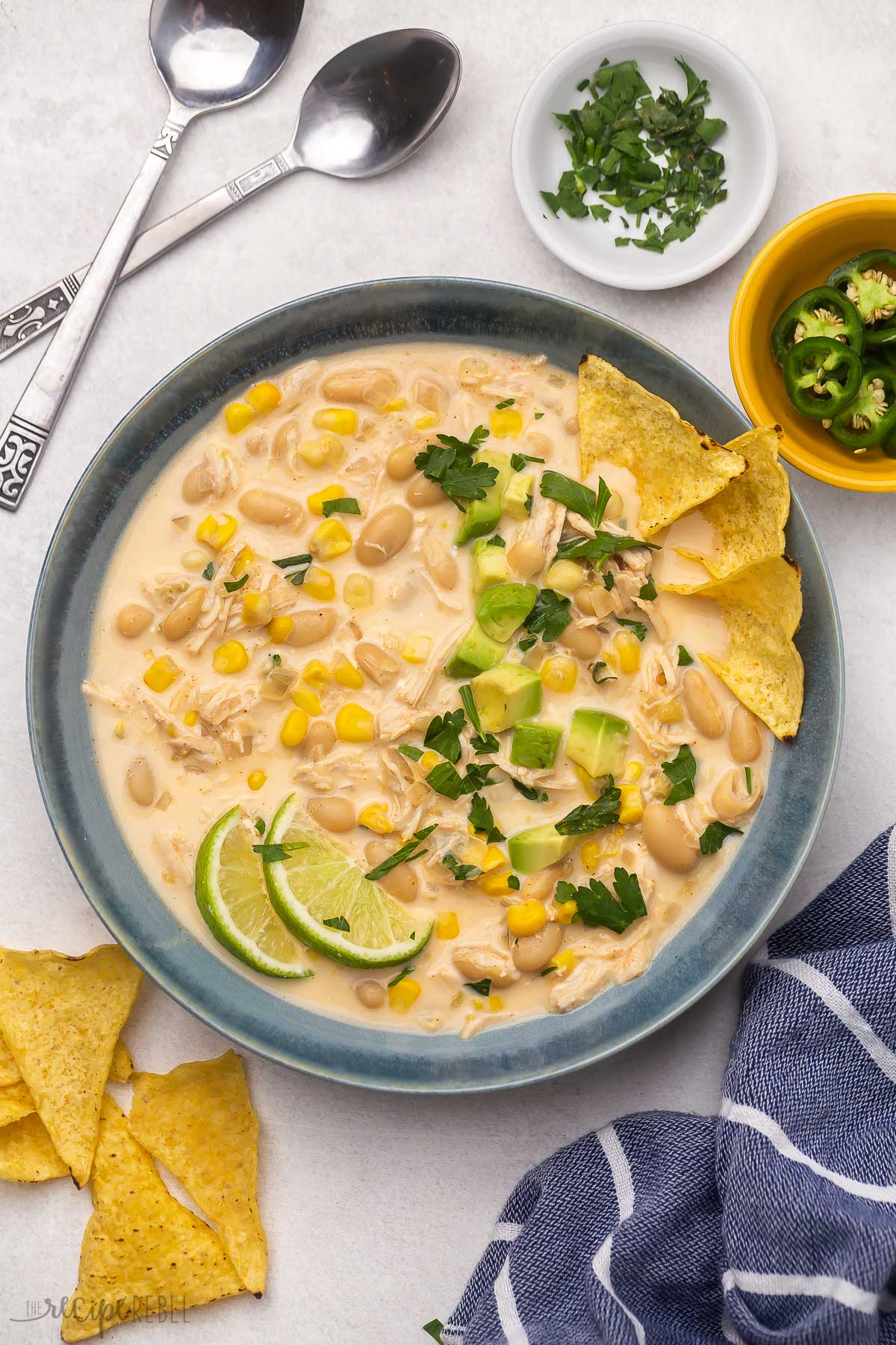 intant pot chicken chili in blue bowl with spoons and toppings beside.