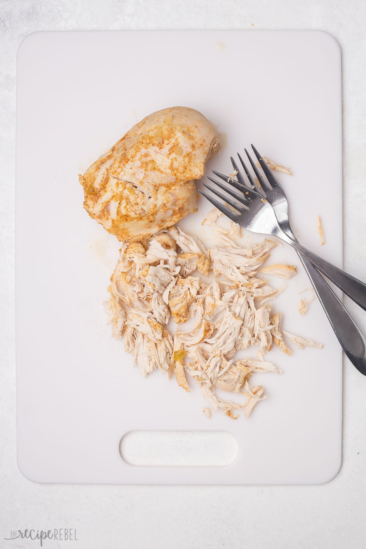 partially shredded chicken breast on a white cutting board with two forks.