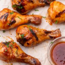 Top view of grilled chicken drumsticks with maple glaze in a glass bowl.