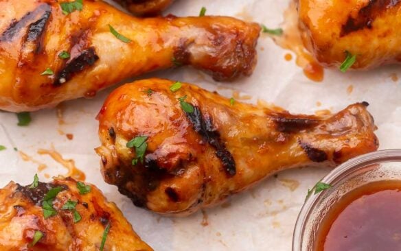 Top view of grilled chicken drumsticks with maple glaze in a glass bowl.