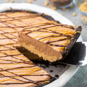 close up of slice of pie with chocolate and peanut drizzled on top.