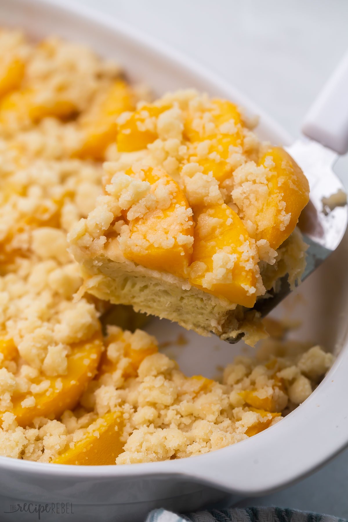 Close up of a slice of peach cobbler french toast being lifted out of a casserole dish. 
