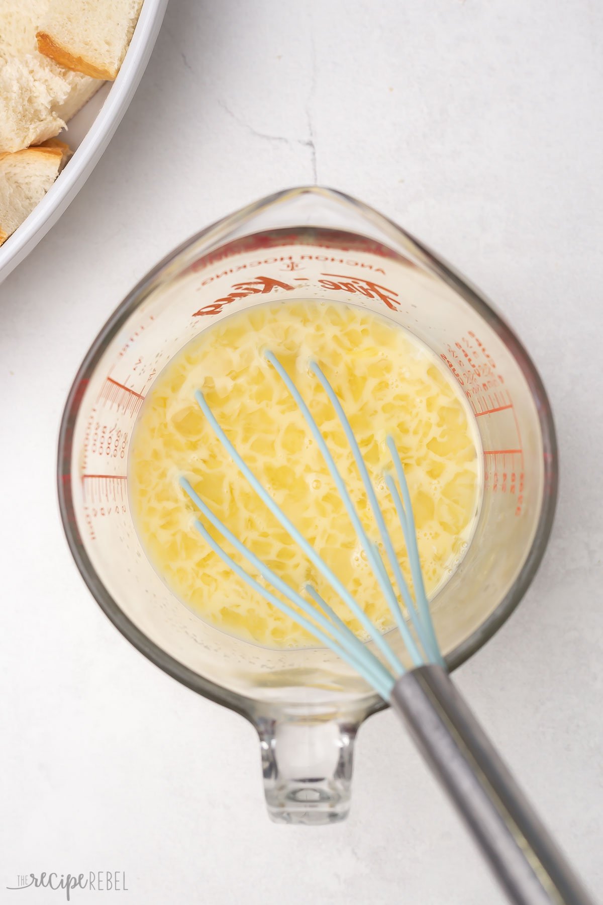 Top view of a glass mixing jug with an egg mixture in it and a whisk sitting in the jug. 