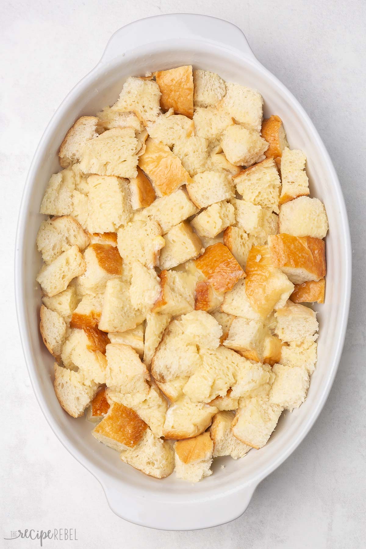 Top view of a casserole dish with bread cubes soaking in an egg mixture. 