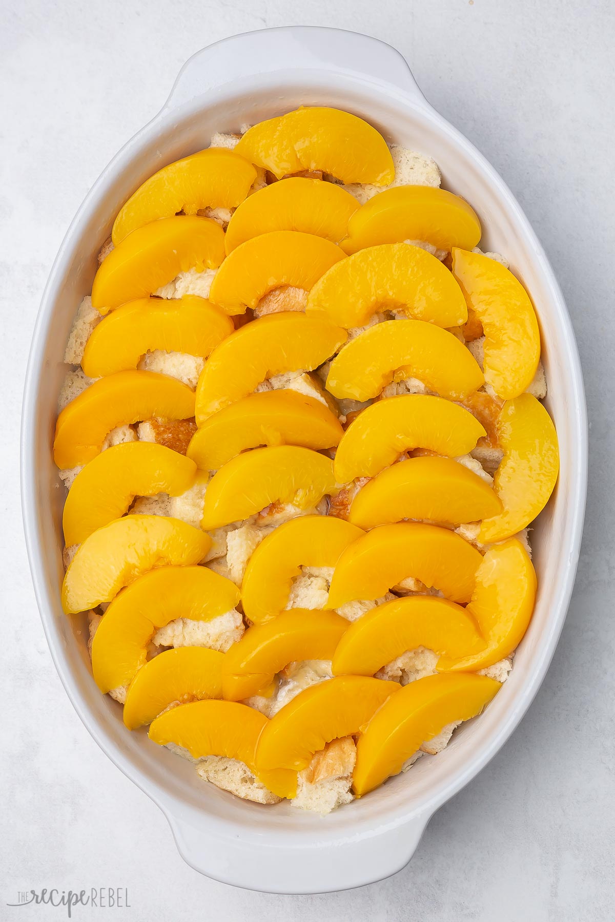 Top view of a casserole dish with peach slices covering bread cubes lined in a single layer.