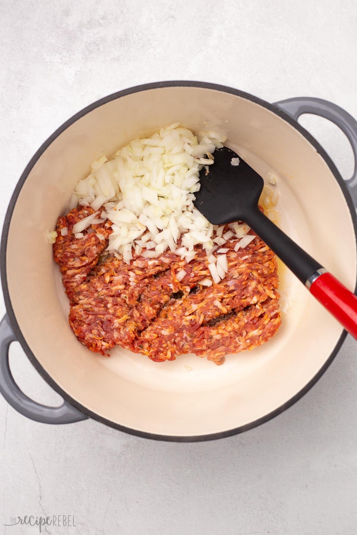 italian sausage, onions and spatula in grey dutch oven.