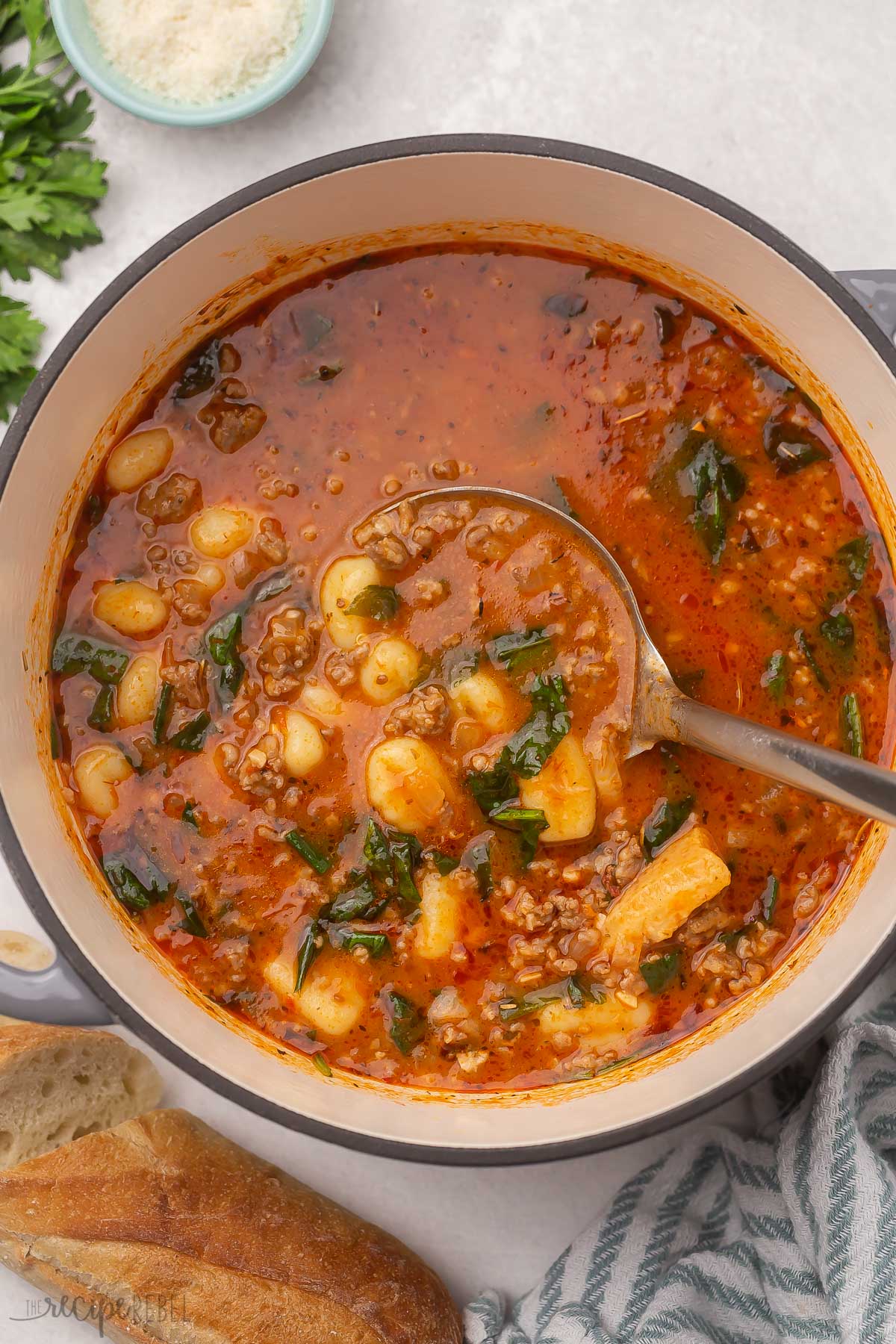 Top view of a large grey pot of sausage gnocchi soup with a metal ladle in it.