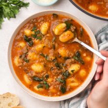 Top view of a spoon scooping some sausage gnocchi soup out of white bowl.