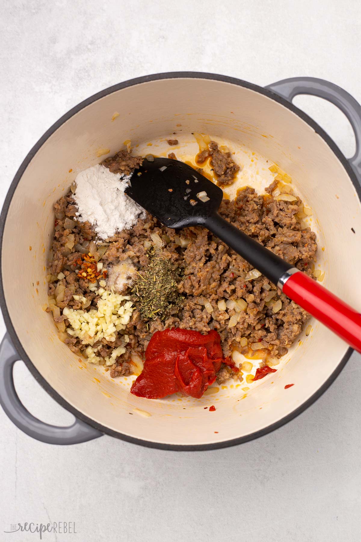 cooked sausage and other ingredients in a dutch oven with red and black spatula.