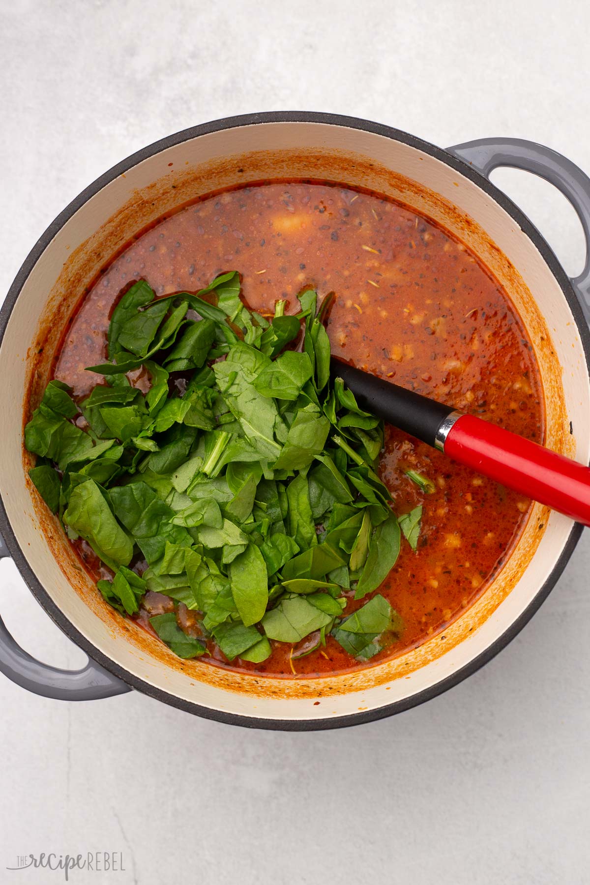 dutch oven full of sausage gnocchi soup with chopped spinach on top.