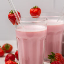 Strawberry milk in two glass cups, glass straws, and strawberries on the rim.