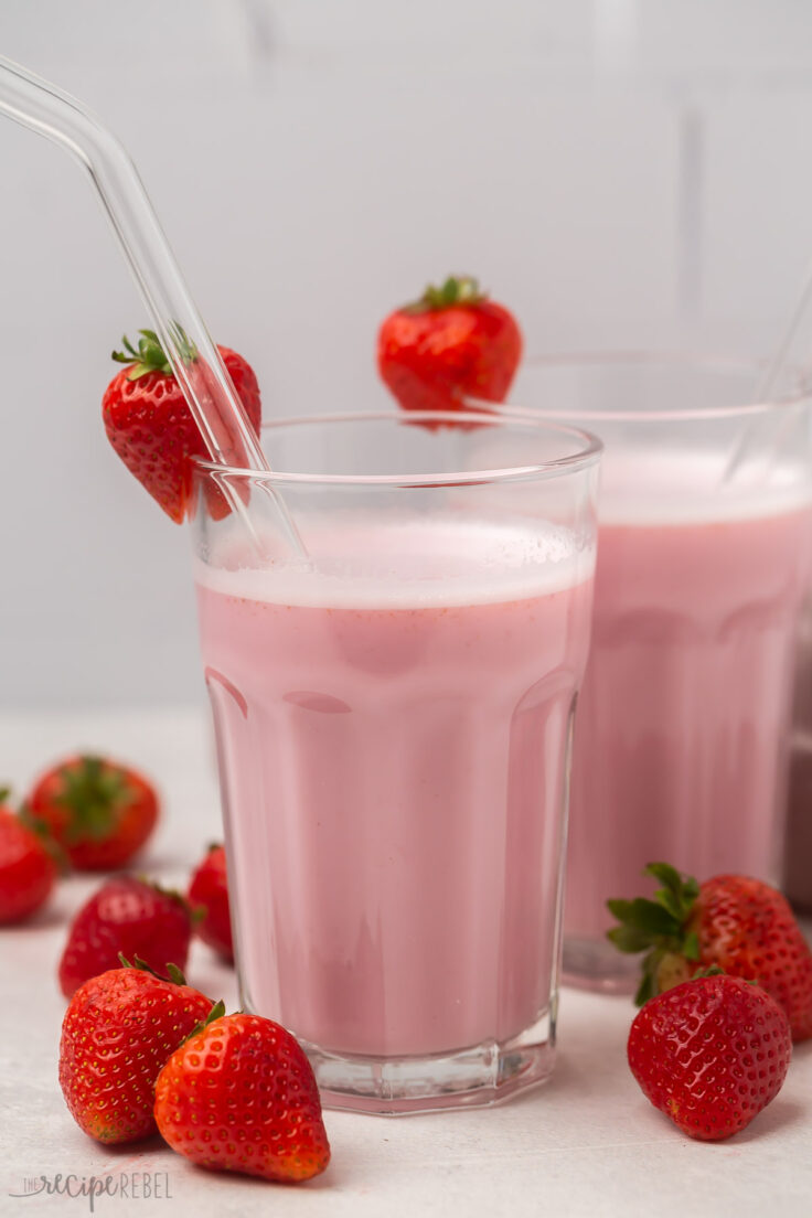 Strawberry milk in two glass cups, glass straws, and strawberries on the rim.
