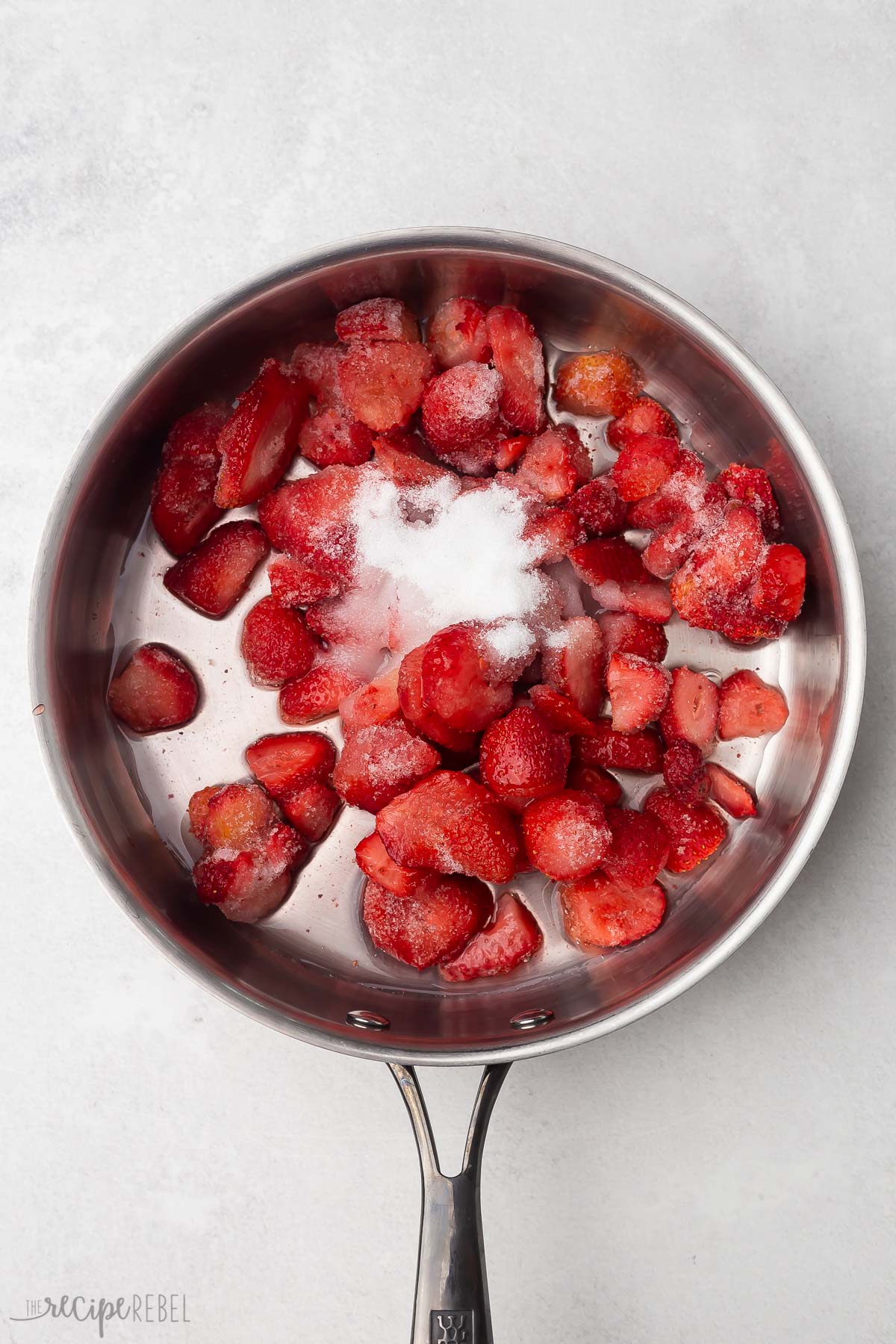 Top view of frozen strawberries, water, and sugar in steel pan.