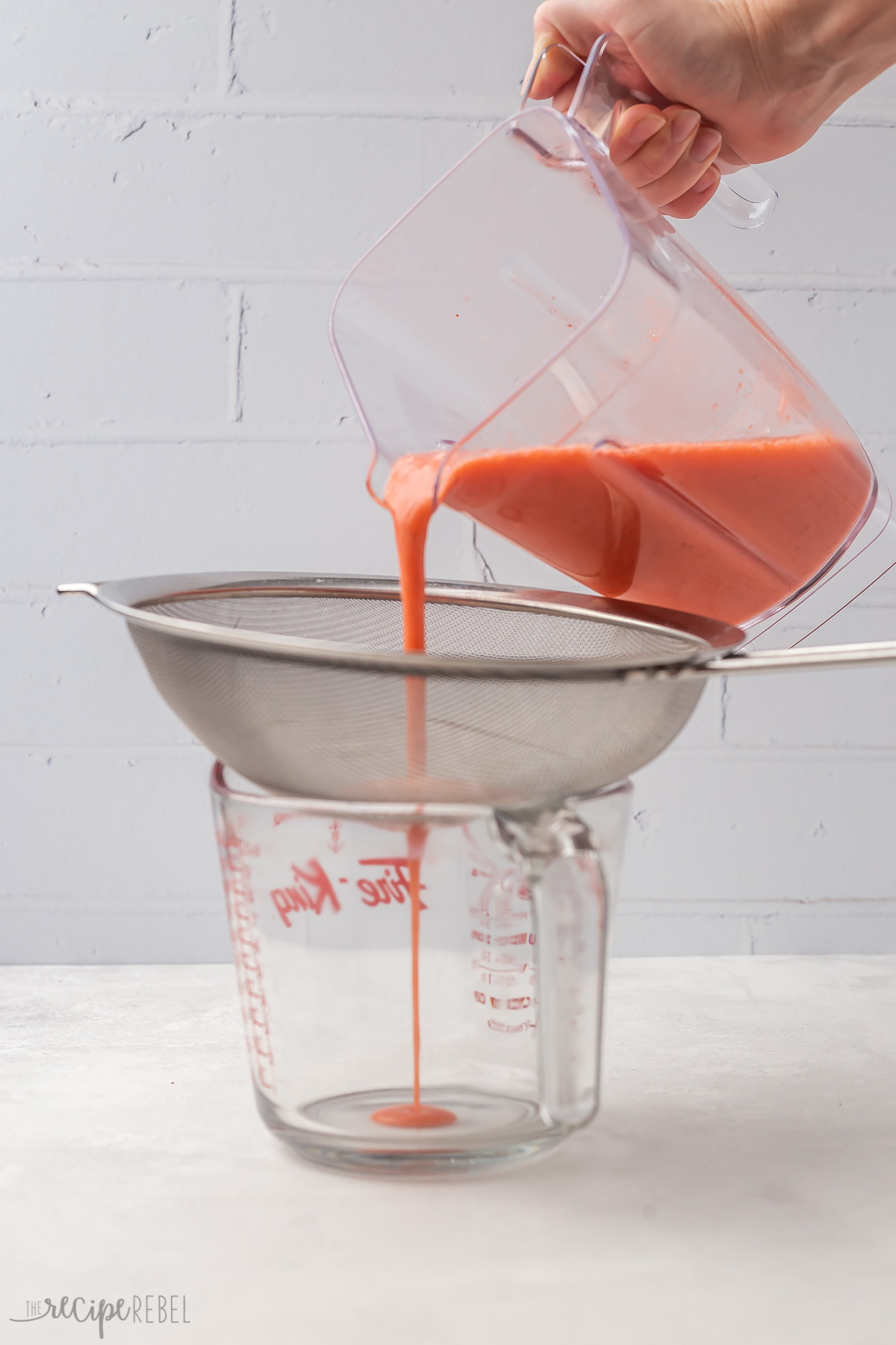 Blended strawberry puree being strained into glass measuring cup.