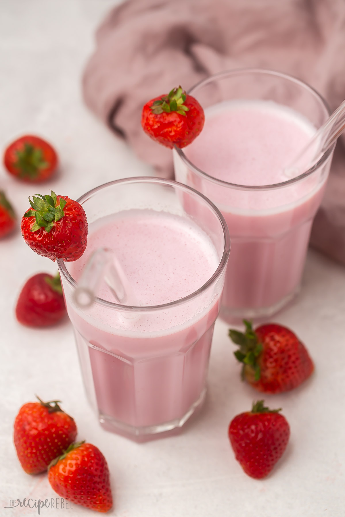 Two glass cups full of strawberry milk with strawberries surrounding them.