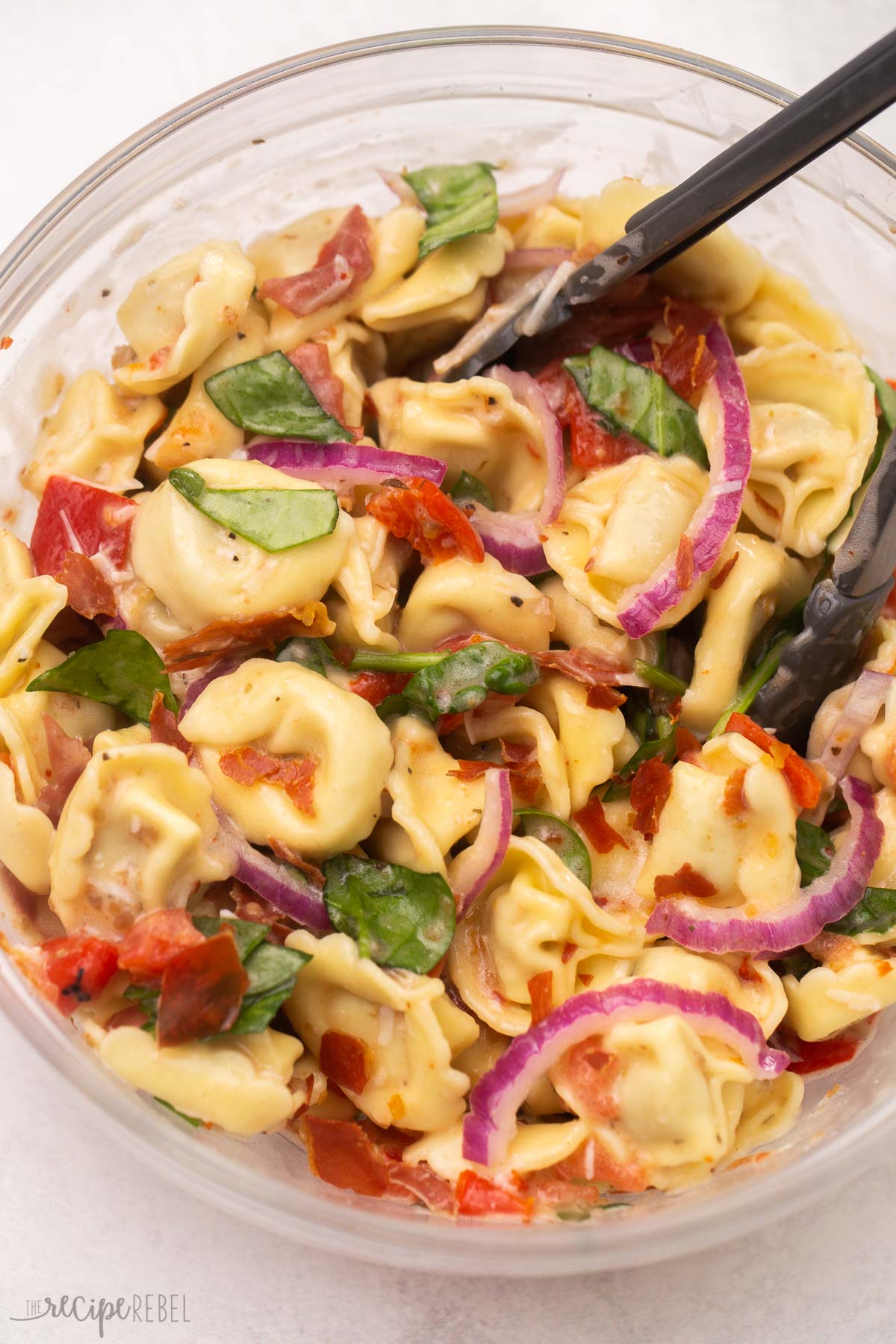 glass bowl full of tortellini pasta salad on grey surface.